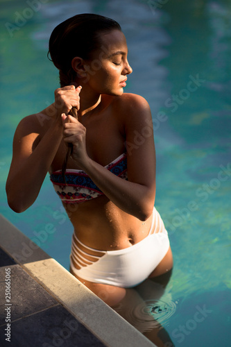 Young woman in bikini posing by the swimming pool outdoor