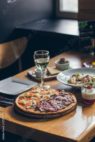 A fresh tasty pizza served with a glass of white wine on the wooden table in the restaurant