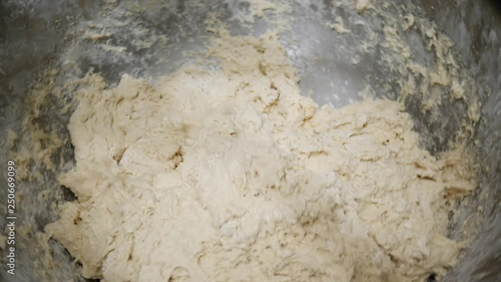 Baker kneads the flour to the new dough for baking in large mechanized aluminum containers Baker kneads the flour to the new dough for baking in large mechanized aluminum containers