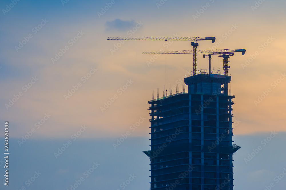 High-rise condominium building under construction in blue and yellow sky background. Silhouette riverfront view of real estate development. High-rise condominium building under construction in blue and yellow sky background. Silhouette riverfront view of real estate development.