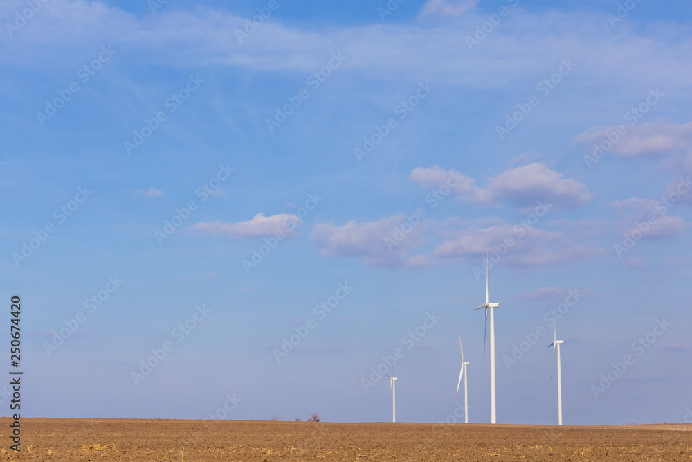 Four windmill turbines on agricultural field with blue sky in background. Renewable energy wind turbine Four windmill turbines on agricultural field with blue sky in background. Renewable energy wind turbine