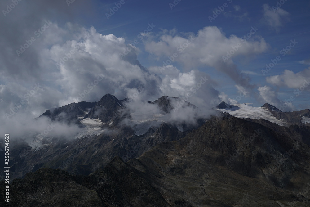 Berglandschaft mit Wolken, Grün, Pflanzen, Felsen und Schnee in Sölden/ Ötztal 