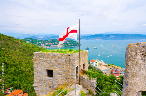 Top aerial view of Gulf of Spezia turquoise water, ancient stone wall of Castello Doria castle tower with flag in Portovenere town, Ligurian sea, Riviera di Levante, La Spezia, Liguria, Italy