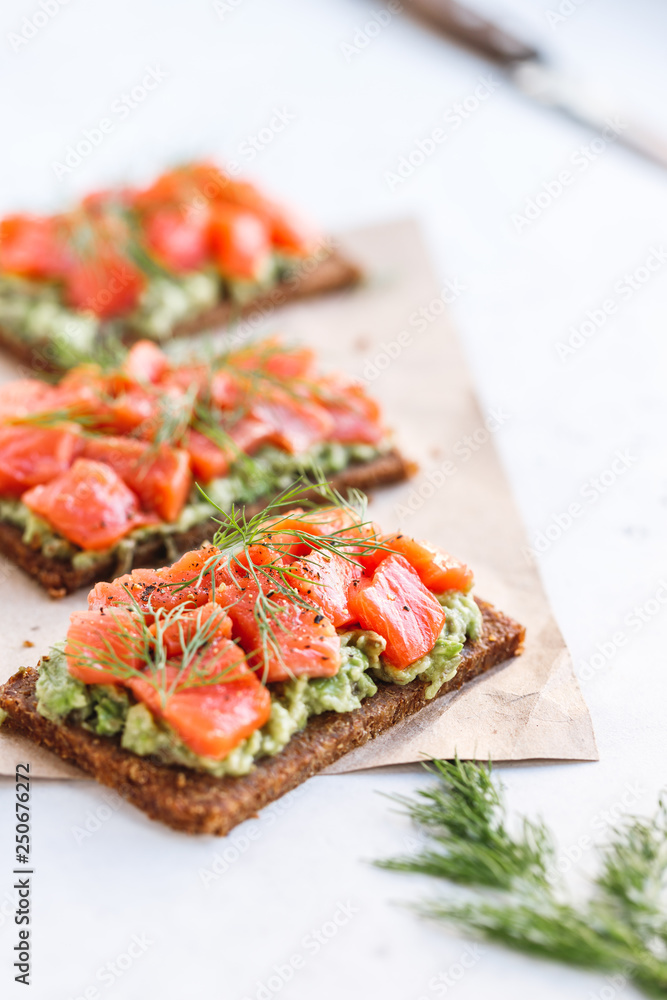 Close-up view of three sandwiches with rye bread, avocado and smoked salmon on a white kitchen table. Close-up view of three sandwiches with rye bread, avocado and smoked salmon on a white kitchen table.