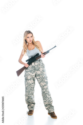 attractive blonde militarywoman in grey t-shirt and camouflage pants standing with rifle isolated on white