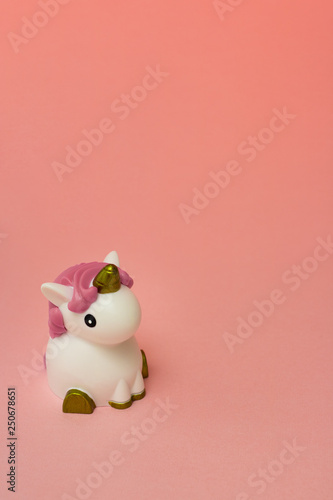 Small cute white unicorn toy with pink hair crest on a coral empty background. Isolated. Copy space. Symbol. Kid. Colour. Vertical