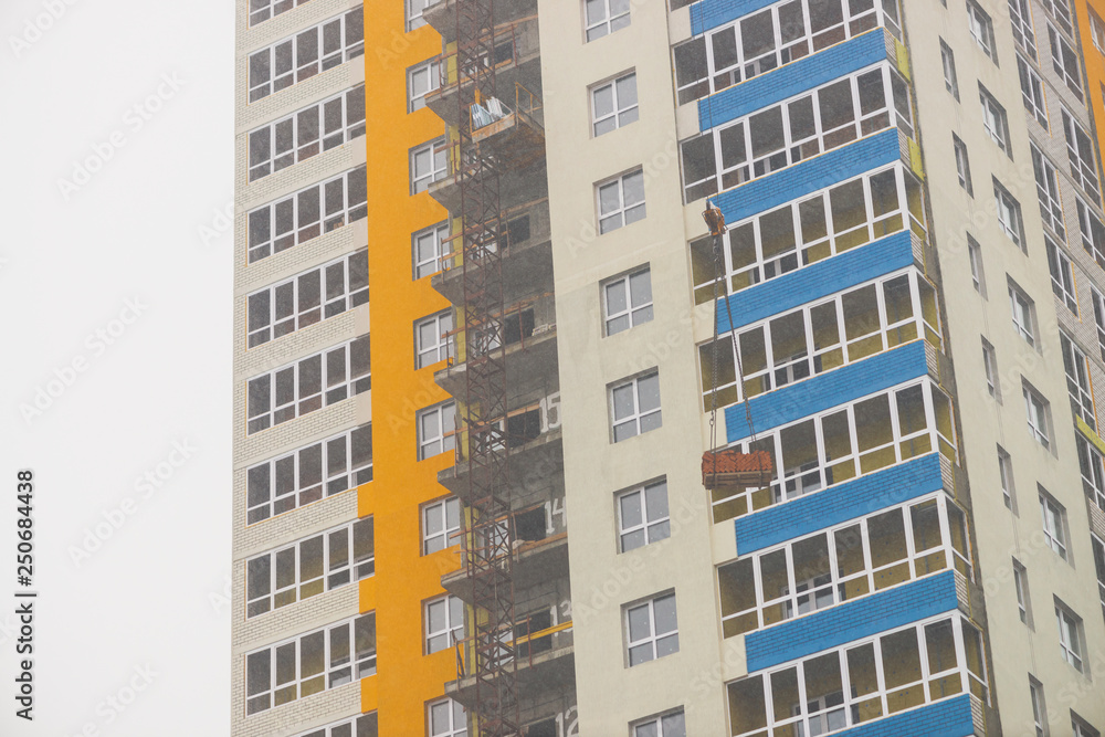 Concept of apartment building under construction close-up. Exterior of multicolor new multi-story residential building. Background with yellow walls, white plastic windows and blue loggias. Copy space