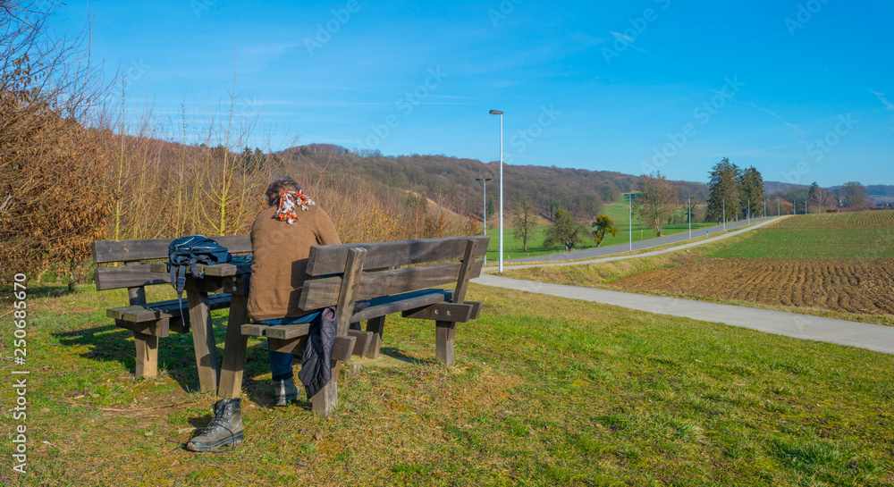 Hiker resting on a wooden bench in a hilly landscape below a blue sky
