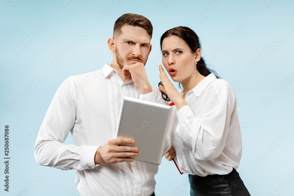 Concept of partnership in business. Young man and woman looking suspicious against blue background at studio Concept of partnership in business. Young man and woman looking suspicious against blue background at studio
