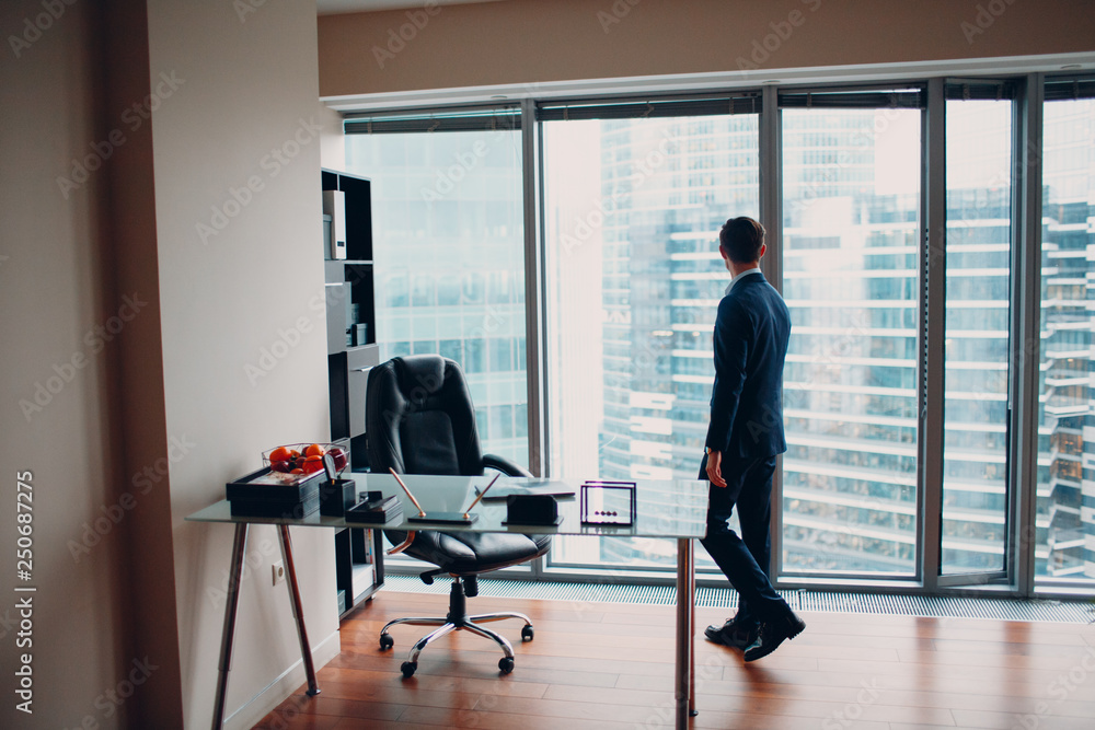 A man in a skyscraper office is standing by a panoramic window. A man in a skyscraper office is standing by a panoramic window.