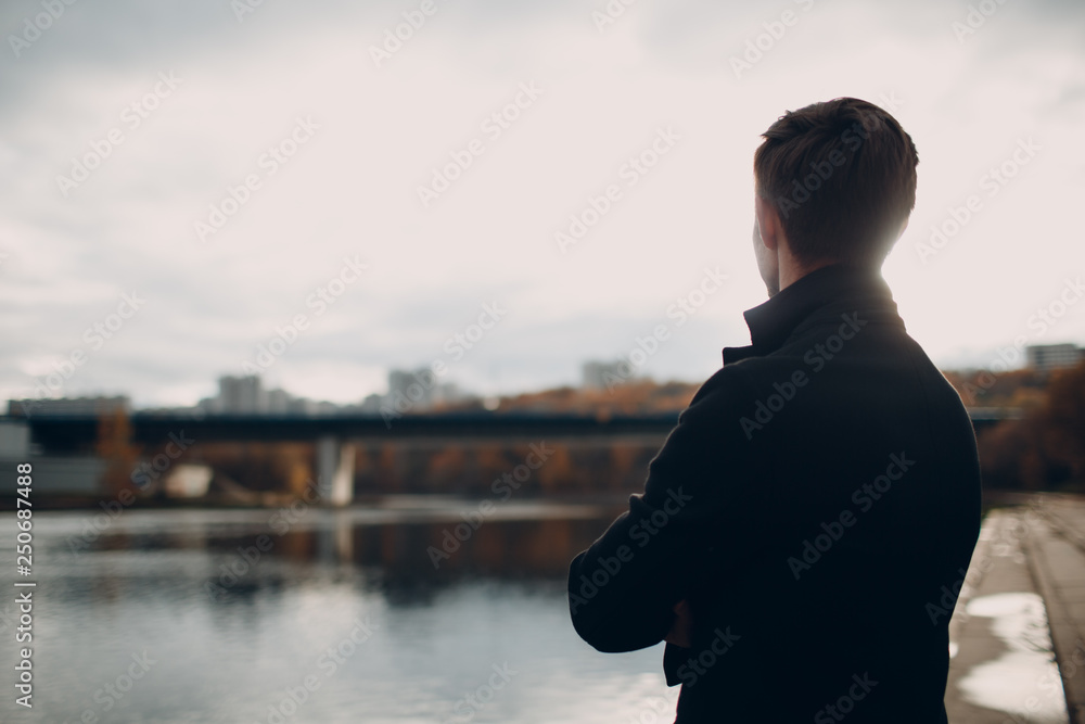 Fototapeta premium The man on the river embankment looks at the houses and the bridge in front of them.