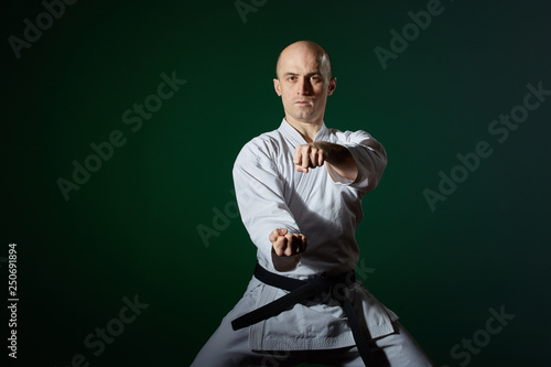 On a dark green background, an athlete in karategi performs formal karate exercises