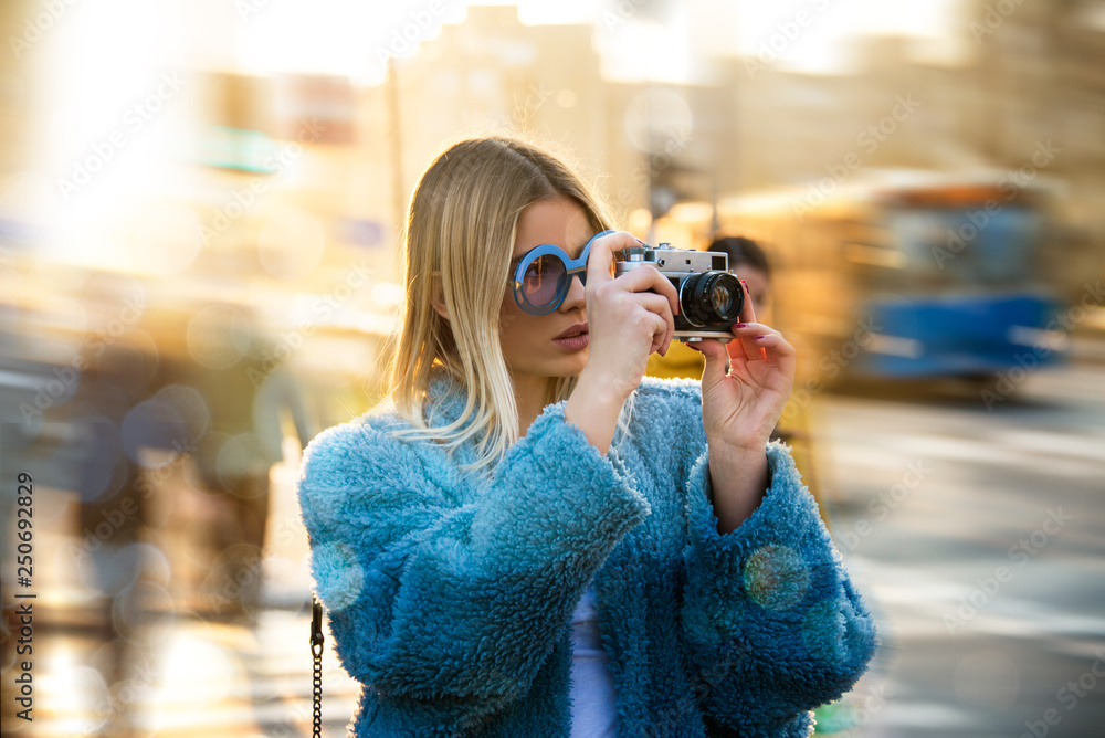 beautiful young blond girl walking down city street in Europe, taking photos with old retro camera hipster Instagram style