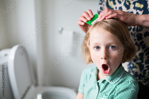 School girl having her hair combed with a comb by her mother