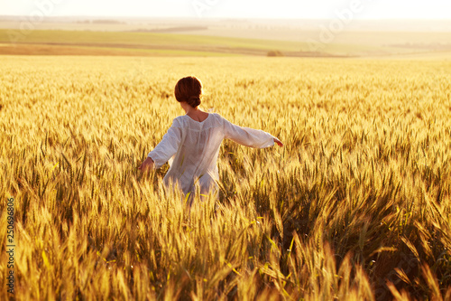 Happy woman walks through a rye field in the rays