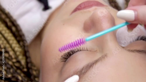 Eyelash Extension Procedure. Woman Eye with Long false Eyelashes. Closeup macro shot of fashion eyes in beauty salon. Hands beautician. Eyelash wizard brushes client's eyelashes with a brush photo