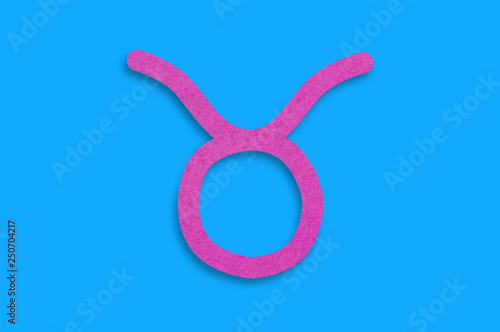 Symbol of astrological sign taurus cut out of purple paper in center on blue table. Top view. Horoscope concept