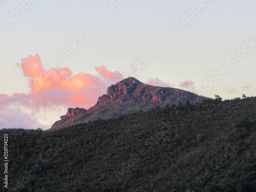 Pôr do sol reflete tons de rosa nas nuvens e montanha.