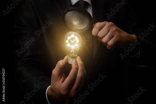 A businessman looking at the lightbulb through the magnifier.