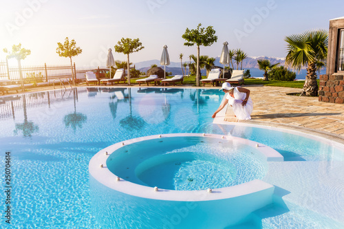 Elegant woman touching the water in a swimming pool. Sunset light, soft focus,best focus at the woman