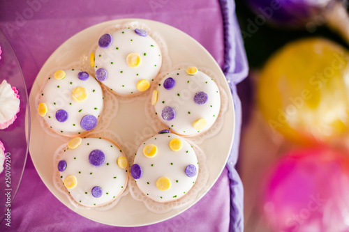 Candy bar for the birthday. White round cakes with big yellow and purple dots and with small green dots. Top view