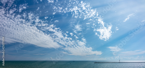 Sky with small clouds over the sea with a breakwater and a beacon