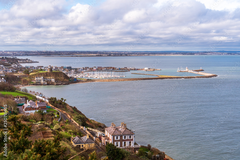 View from the Howth Head peak over the beautiful fishing village of Howth with a distant small defensive fort keeping watch over the harbor. City landscape in County Dublin, Ireland.