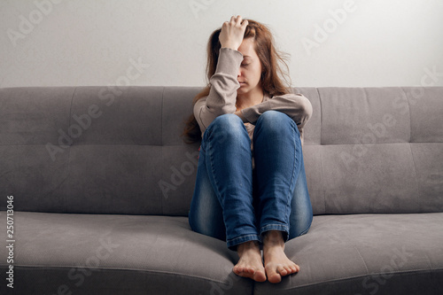 Frustrated girl sitting on the couch with a headache.