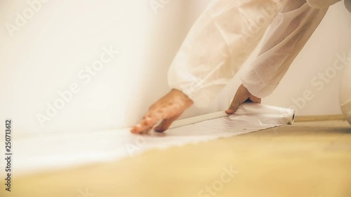 Taping plastic sheet to the edge of floor. Low angle close-up of person hands in focus taping down a protective sheet to the floor.