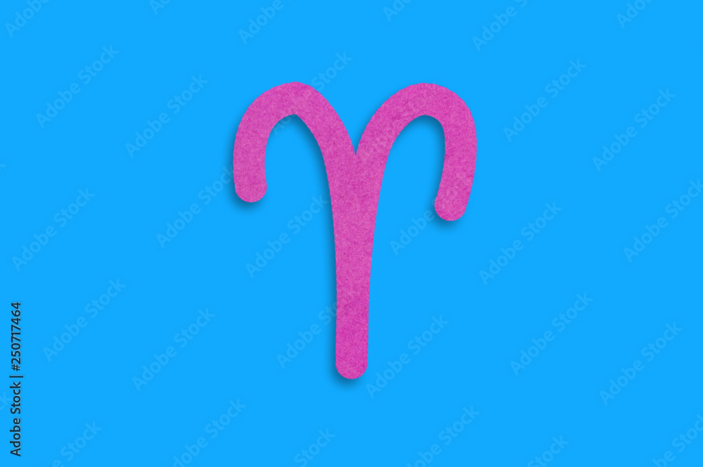 Symbol of astrological sign aries cut out of purple paper in center on blue table. Top view. Horoscope concept Symbol of astrological sign aries cut out of purple paper in center on blue table. Top view. Horoscope concept
