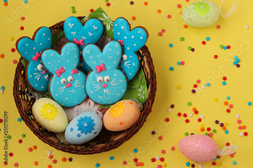 Easter funny blue rabbits, homemade painted gingerbread biscuits in glaze in a wicker basket on a yellow background, Top view