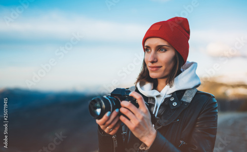 hipster tourist girl hold in hands take photography click on modern photo camera, photographer look on camera technology, journey landscape vacation concept, sun flare mountain photo