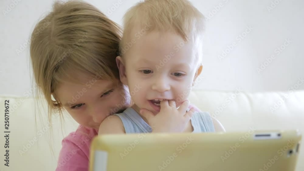 Adorable little brother and sister using digital tablet, smiling and looking happy. Brother and sister having fun at home. Adorable little brother and sister using digital tablet, smiling and looking happy. Brother and sister having fun at home.