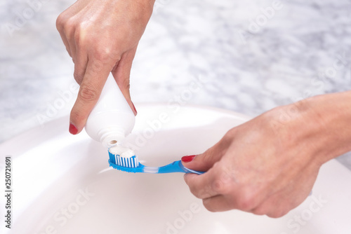 Woman holding a tooth brush putting toothpaste on it .