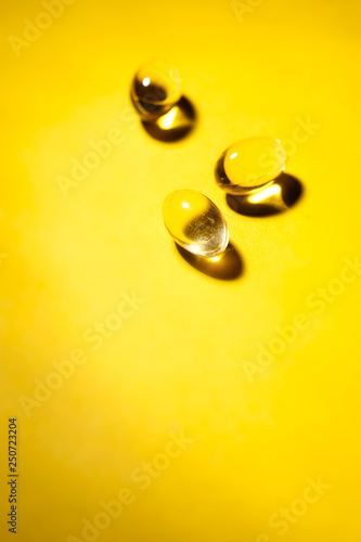 Yellow transparent pills on yellow background. Vertical image