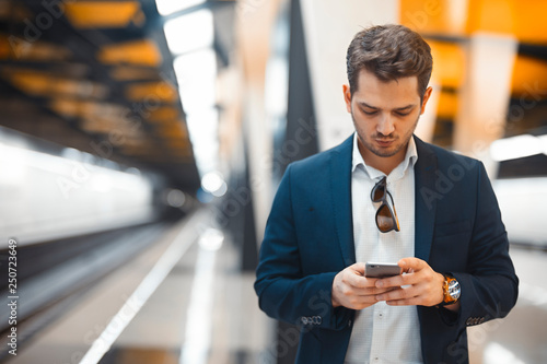 Attractive businessman texting message in mobile phone while waiting for train in metro.