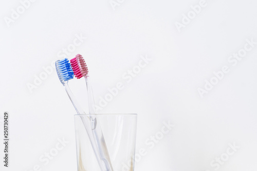A glass with two plastic toothbrushes of pink and blue color on white and wooden background. Love and tooth hygiene concept.