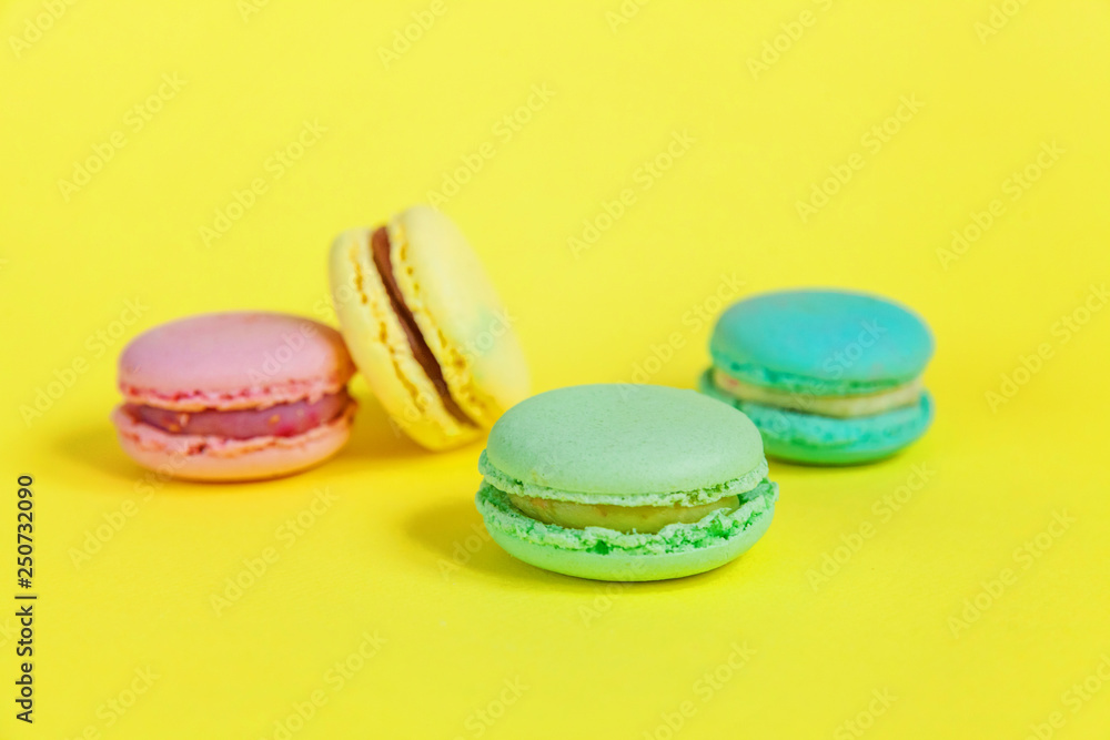 Obraz premium Sweet almond colorful unicorn pink blue yellow green macaron or macaroon dessert cake isolated on trendy yellow modern fashion background. French sweet cookie. Minimal food bakery concept. Copy space