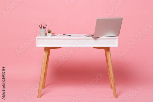 Office light interior of workplace, white table desk with modern laptop pc computer, documents orange notebook pencils, flower isolated on pastel pink wall background in studio. Accessories concept.