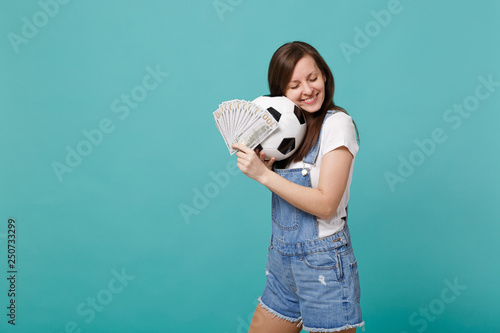 Tender young girl football fan with closed eyes support favorite team with soccer ball, fan of money in dollar banknotes cash money isolated on blue turquoise background. Sport family leisure concept. photo