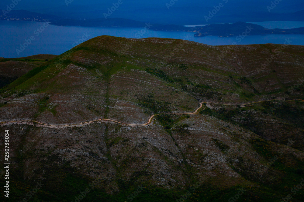 Fototapeta premium Aerial view of beautiful green mountain with road on it. Nature concept with scenic view of hill with blue sky