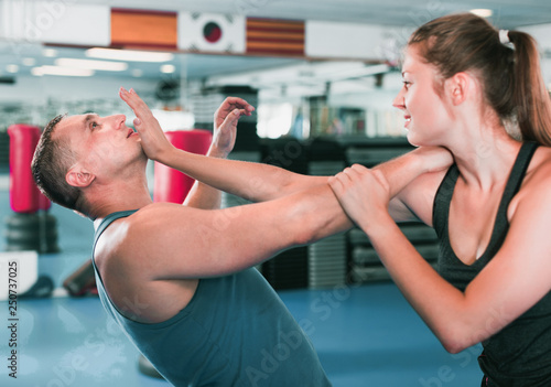 Kobieta trenuje z mężczyzną na kursie samoobrony w siłowni.