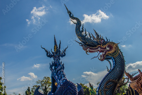 Beautiful blue naga sculpture with blue sky and white cloud on the sunny day at the public temple, Wat Rong Sua Ten, Chiang Rai, Thailand. Naga is a very great snake, found in the Buddhism temples.