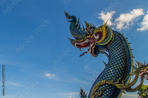 Beautiful blue naga sculpture with blue sky and white cloud on the sunny day at the public temple, Wat Rong Sua Ten, Chiang Rai, Thailand. Naga is a very great snake, found in the Buddhism temples. © kampwit