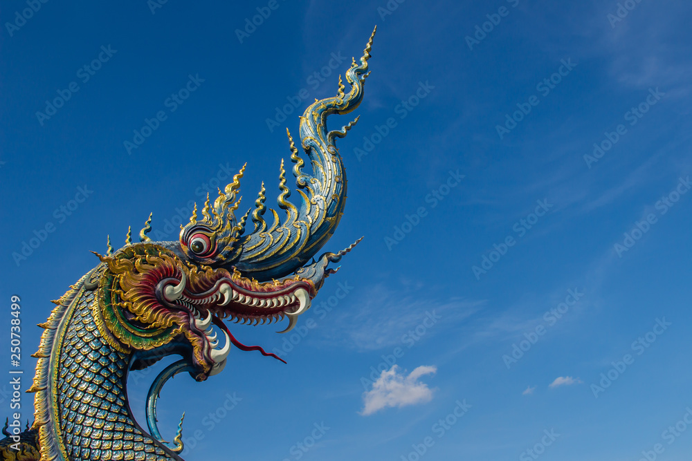 Fototapeta premium Beautiful blue naga sculpture with blue sky and white cloud on the sunny day at the public temple, Wat Rong Sua Ten, Chiang Rai, Thailand. Naga is a very great snake, found in the Buddhism temples.