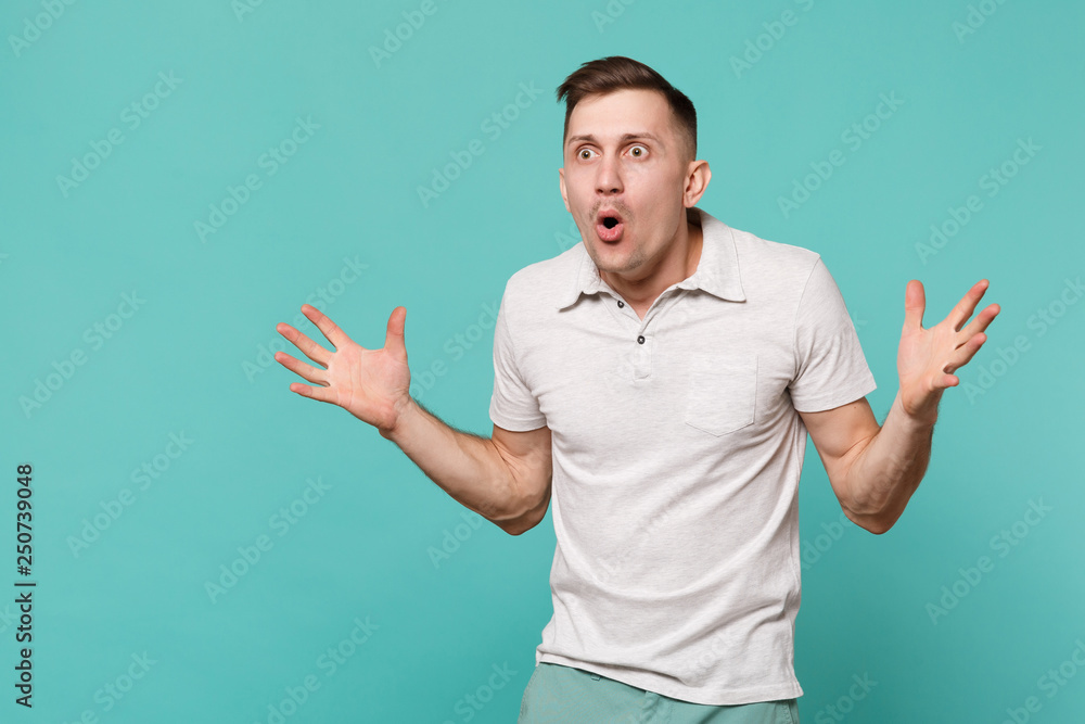 Portrait of amazed shocked young man in casual clothes standing and spreading hands isolated on blue turquoise wall background in studio. People sincere emotions lifestyle concept. Mock up copy space. Portrait of amazed shocked young man in casual clothes standing and spreading hands isolated on blue turquoise wall background in studio. People sincere emotions lifestyle concept. Mock up copy space.