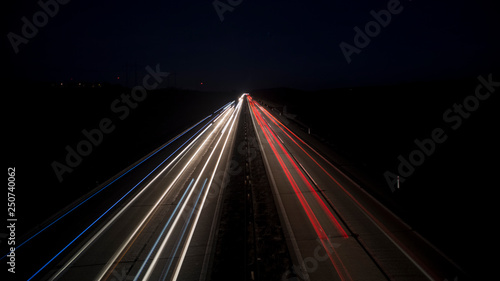 Night urban scene of motion blurred light tracks glowing to the darkness of highway traffic transport to the city just after sunset. Creative long time exposure diagonal composed photography.