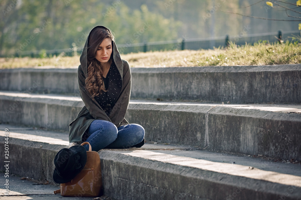 Beautiful unhappy woman sitting alone on staircase outdoors.