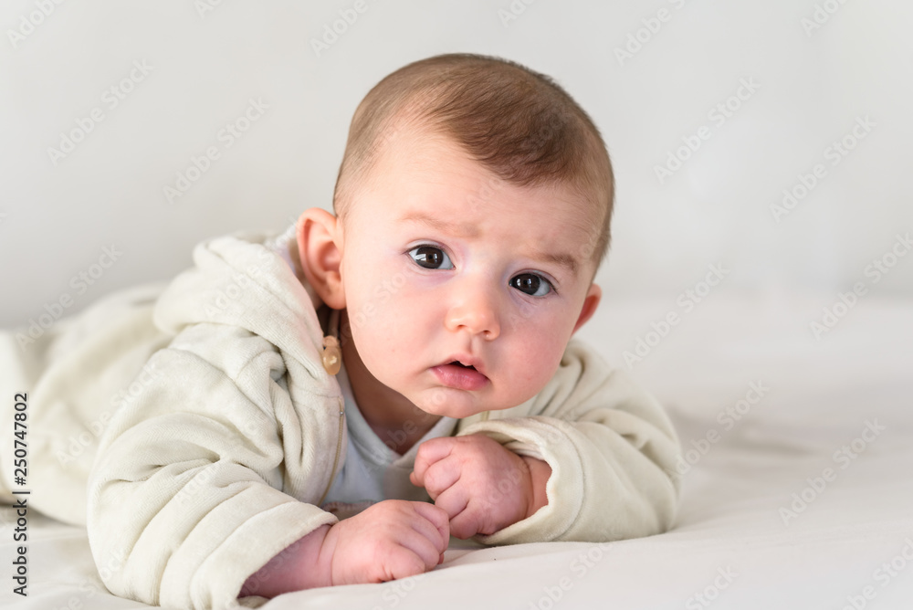 Beautiful and sweet newborn baby lying face down on the bed raising his head to look at the camera curiously. Beautiful and sweet newborn baby lying face down on the bed raising his head to look at the camera curiously.