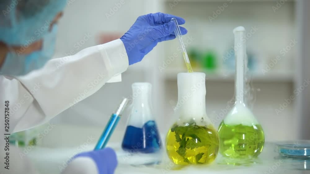 Biochemist dripping organic liquid from flask with plant in tube with blue agent Biochemist dripping organic liquid from flask with plant in tube with blue agent